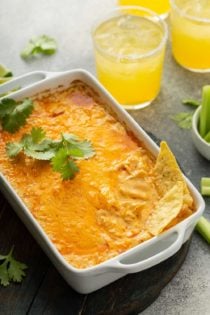 Tortillas sticking out of a buffalo chicken dip in a white casserole dish, with margaritas in the background