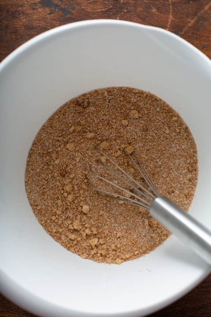 Spices and sugar for apple butter being whisked together in a white bowl