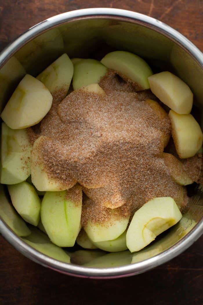 Peeled, cored, and quartered apples in the bowl of an instant pot, topped with sugar and spices for making apple butter