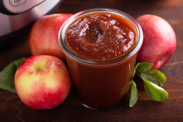 Glass jar filled with apple butter, surrounded by apples