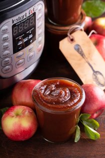 Glass gar filled with apple butter, with apples and an instant pot in the background