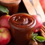 Glass jar filled with apple butter, with apples and more jars of apple butter in the background