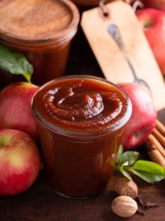 Glass jar filled with apple butter, with apples and more jars of apple butter in the background