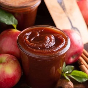 Glass jar filled with apple butter, with apples and more jars of apple butter in the background