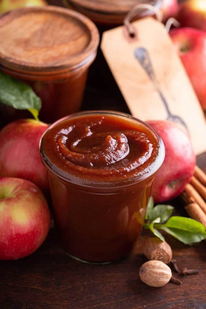Glass jar filled with apple butter, with apples and more jars of apple butter in the background