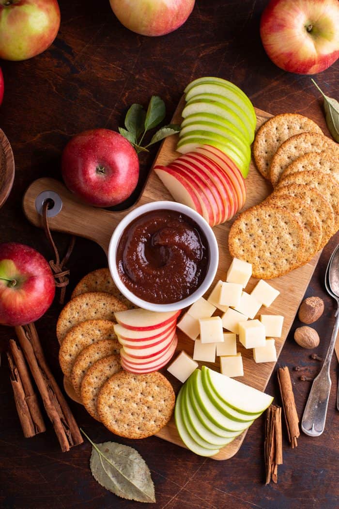 Overhead view of a board filled with crackers, cheese, sliced apples and a small bowl of apple butter