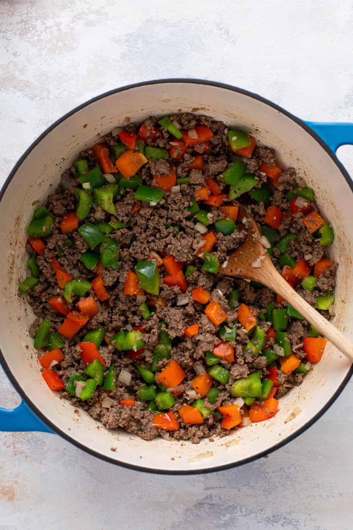 Ground beef, chopped bell peppers and chopped onion cooked in a blue dutch oven.