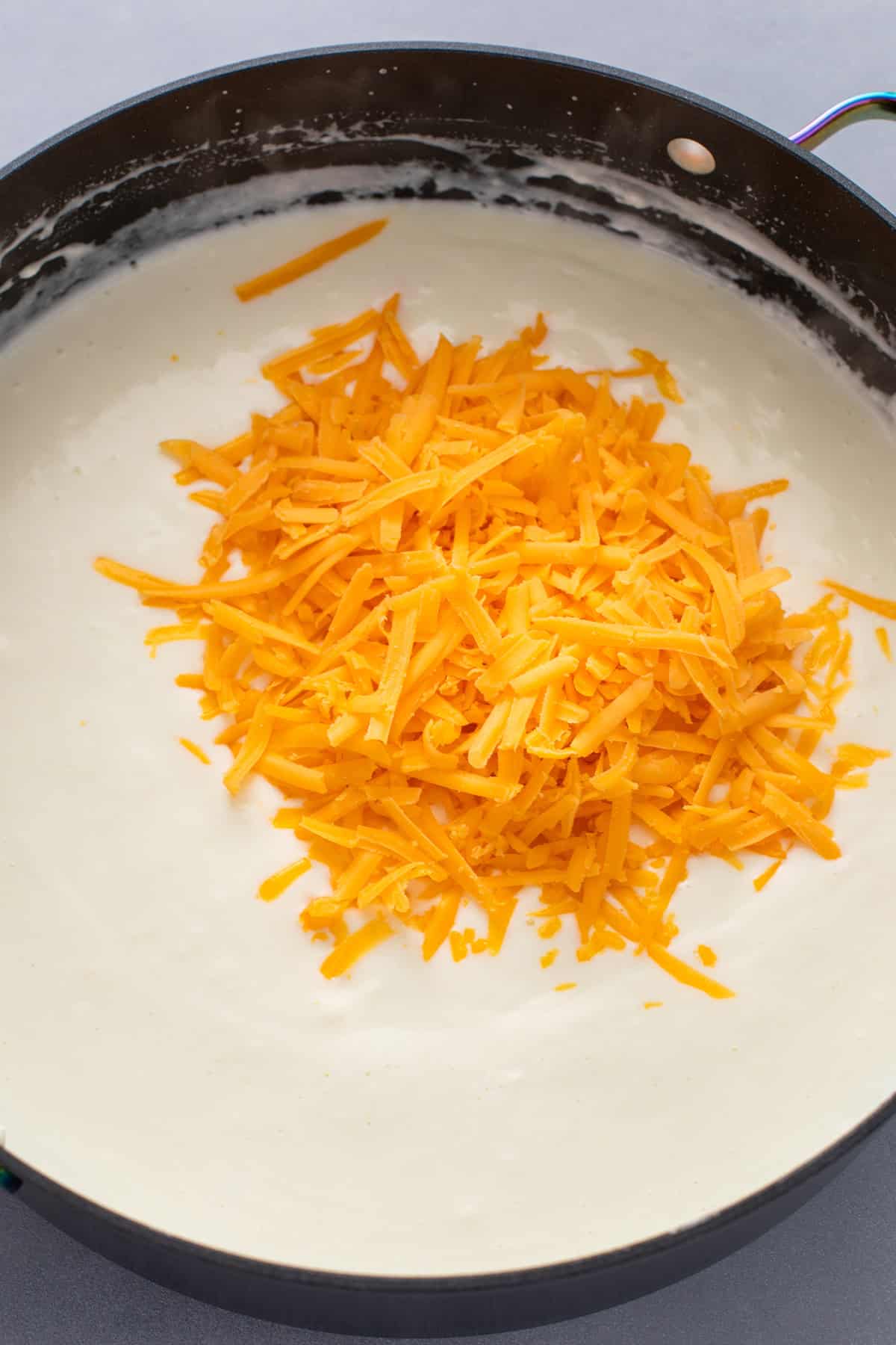 Shredded cheese being added to sauce for mac and cheese.