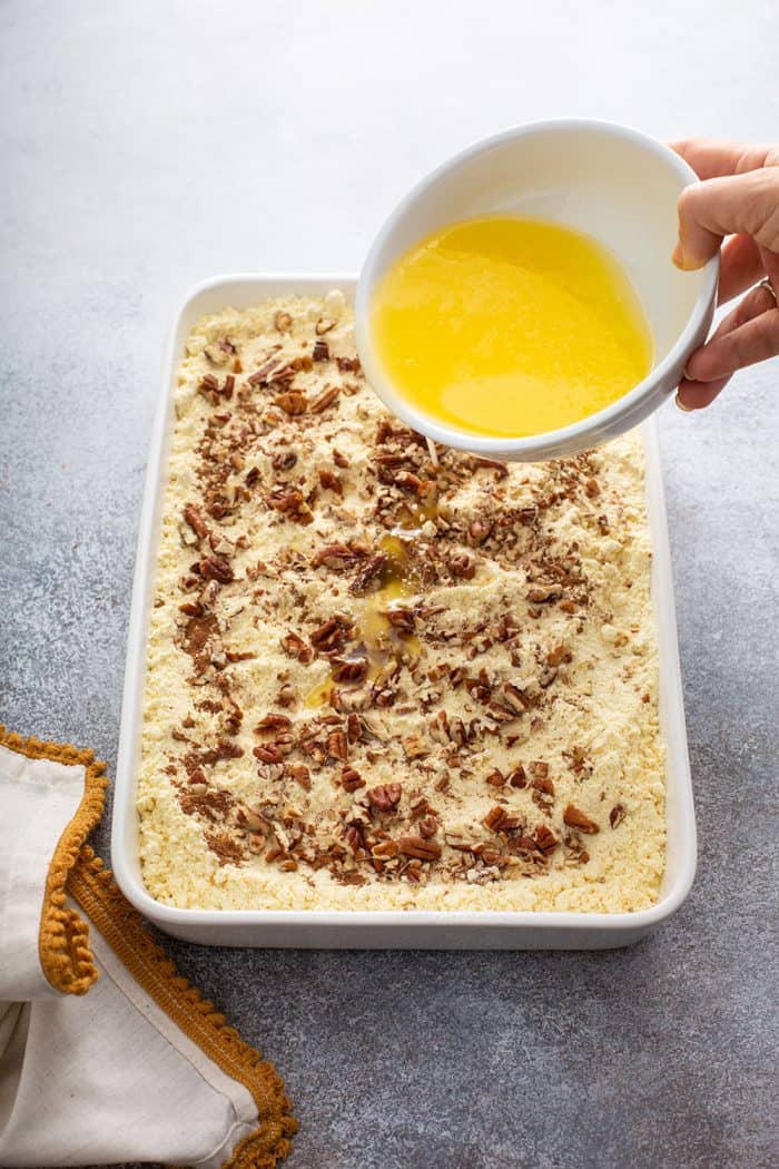 hand pouring melted butter from a bowl on top of cake mix for apple dump cake