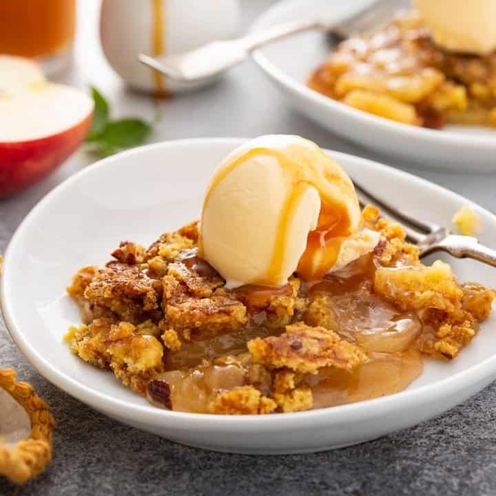 Slice of apple dump cake on a plate topped with vanilla ice cream and caramel sauce