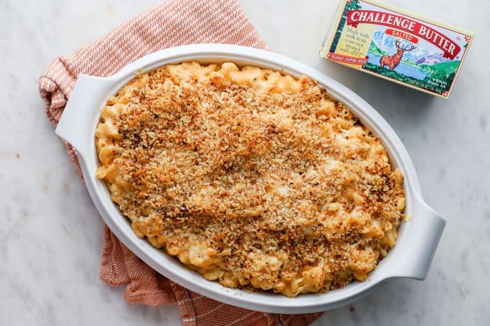 White casserole dish of baked macaroni and cheese set on a pink dish towel on a marble counter