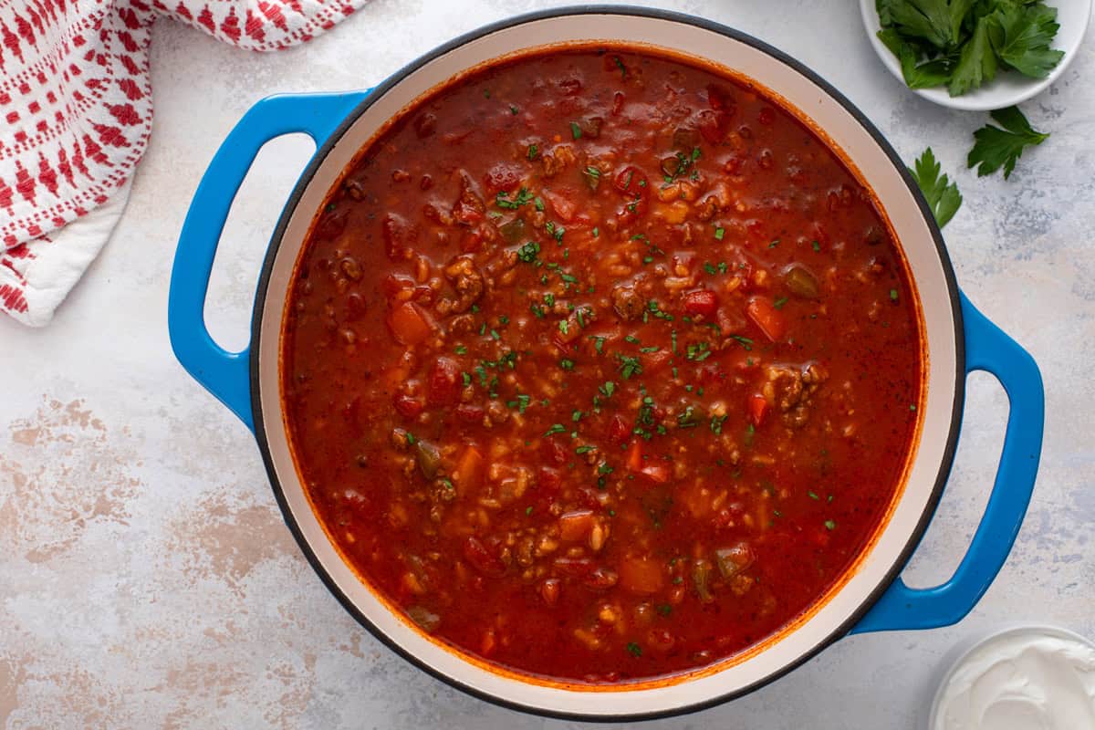 Overhead view of stuffed pepper soup topped with fresh parsley in a blue dutch oven.