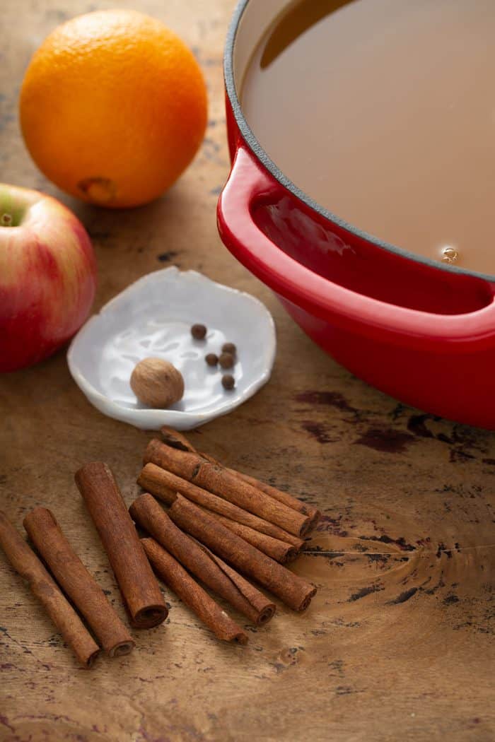 Orange, apple, and whole spices next to a red dutch oven