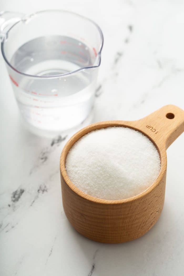 Measuring cups of water and sugar on a marble counter