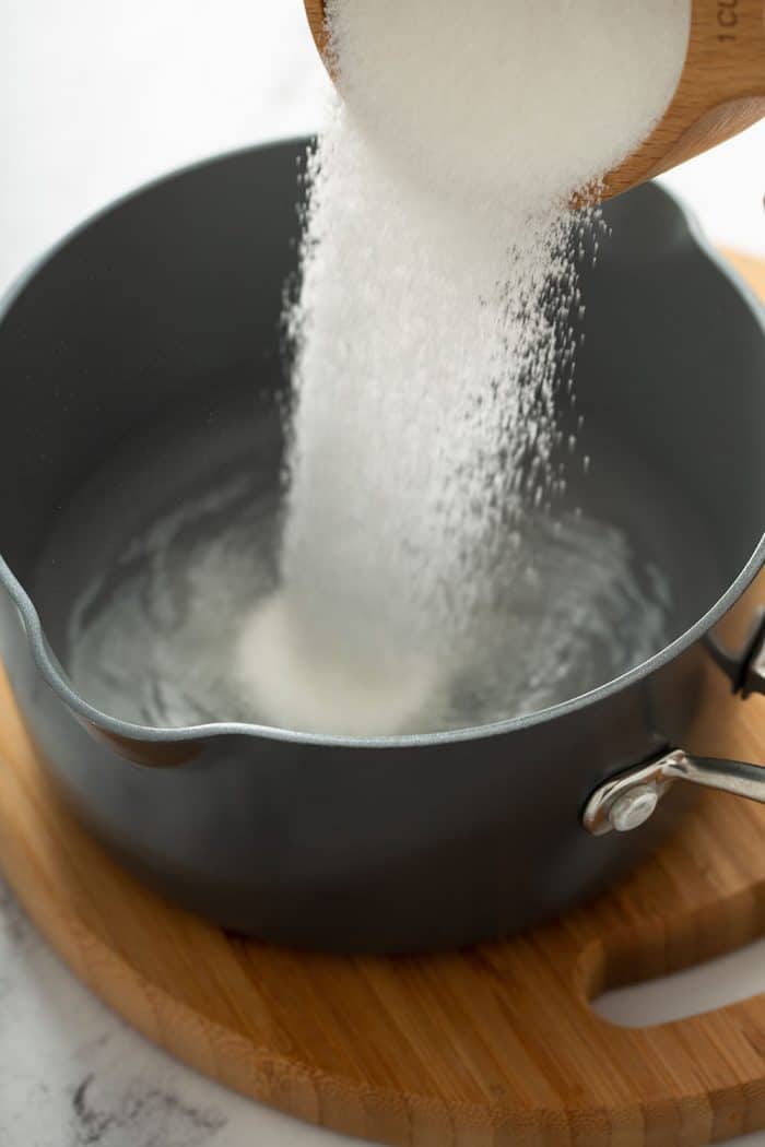 Measuring cup pouring sugar into a saucepan