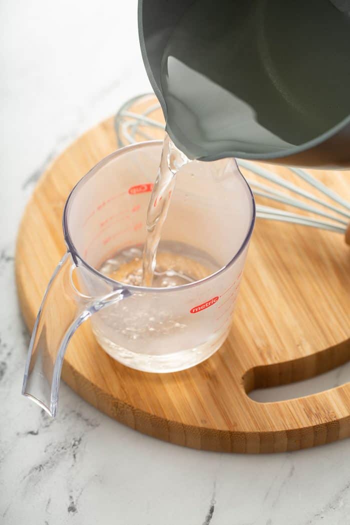 Sauce pan pouring simple syrup into a measuring cup