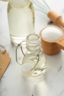Small glass bottle of simple syrup on a marble counter with a measuring cup of sugar