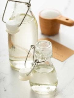 A large and small bottle of simple syrup with a measuring cup of sugar in the background