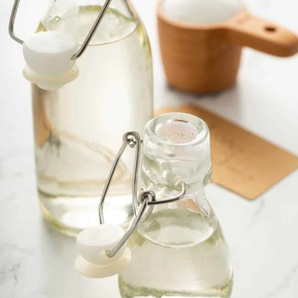 A large and small bottle of simple syrup with a measuring cup of sugar in the background