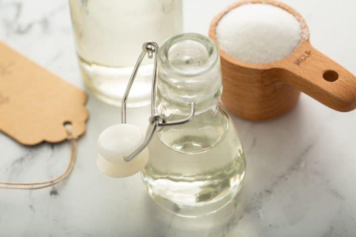 Glass bottle of simple syrup in front of a jar and a measuring cup of sugar