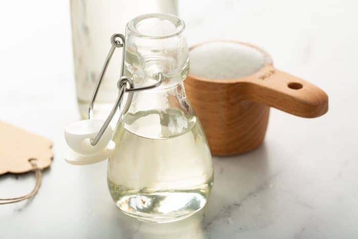 Glass bottle of simple syrup next to a measuring cup of sugar on a marble counter