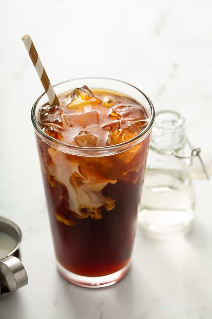 Glass of iced coffee next to a glass bottle of simple syrup