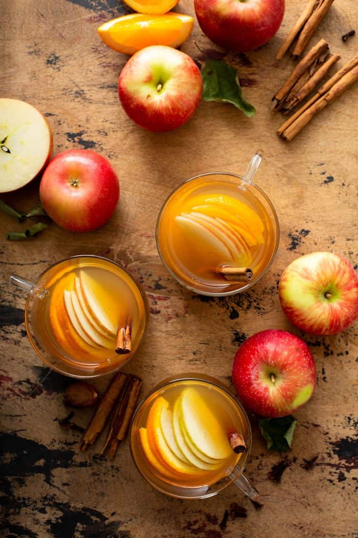 Overhead view of three mugs of wassail surrounded by apples and cinnamon sticks