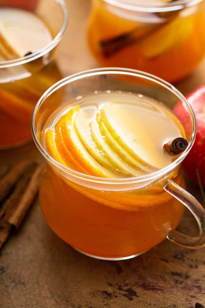 Close up of glass mug of wassail with sliced apples and a cinnamon stick in it