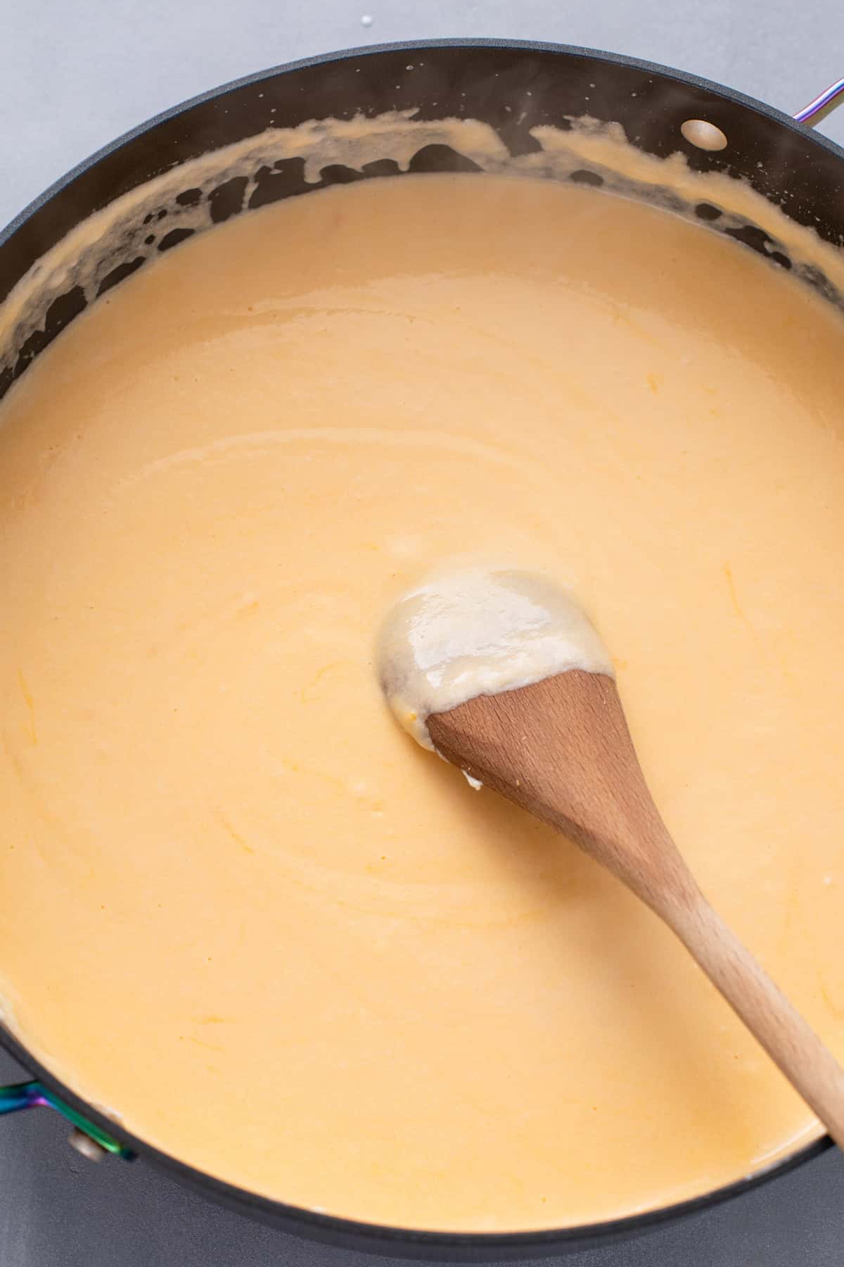 Wooden spoon stirring cheese sauce for baked macaroni and cheese.