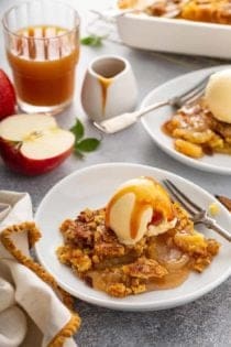 Two shallow bowls filled with apple dump cake topped with vanilla ice cream and caramel sauce