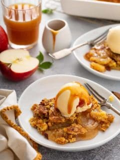 Two shallow bowls filled with apple dump cake topped with vanilla ice cream and caramel sauce