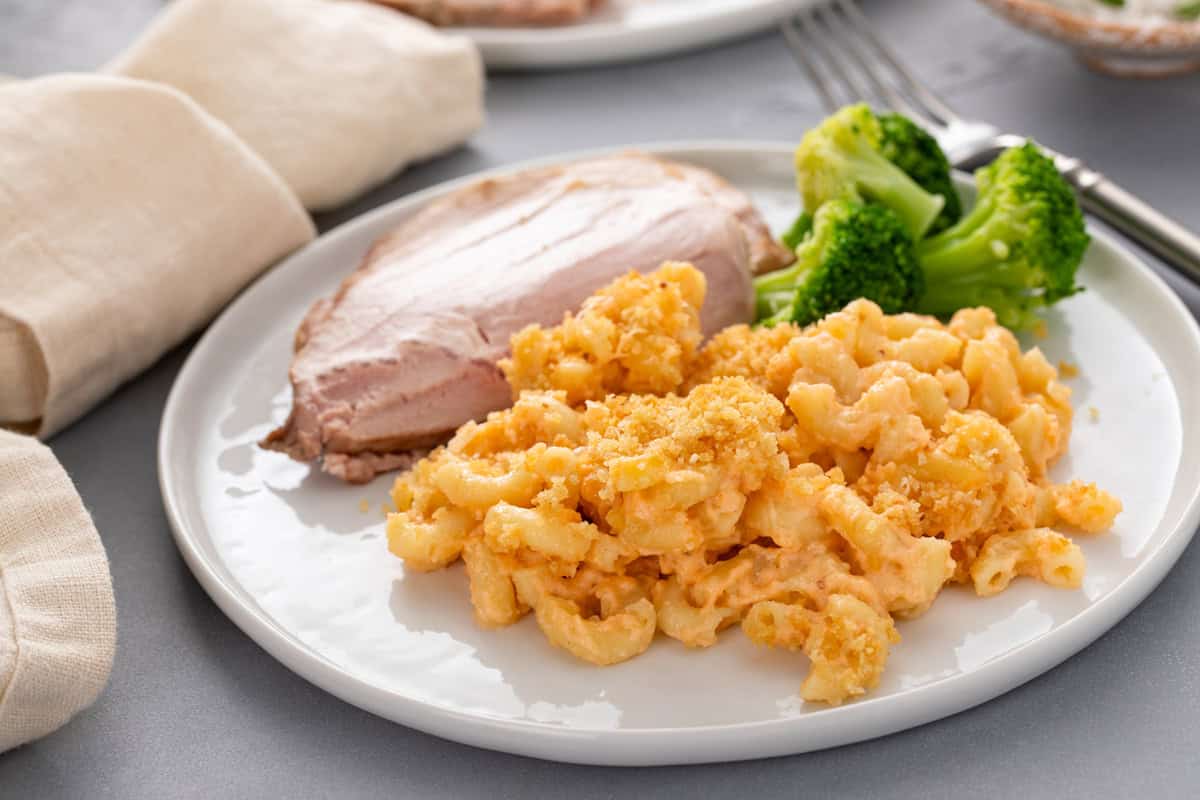 White plate holding slices of turkey and steamed broccoli next to a serving of baked macaroni and cheese.
