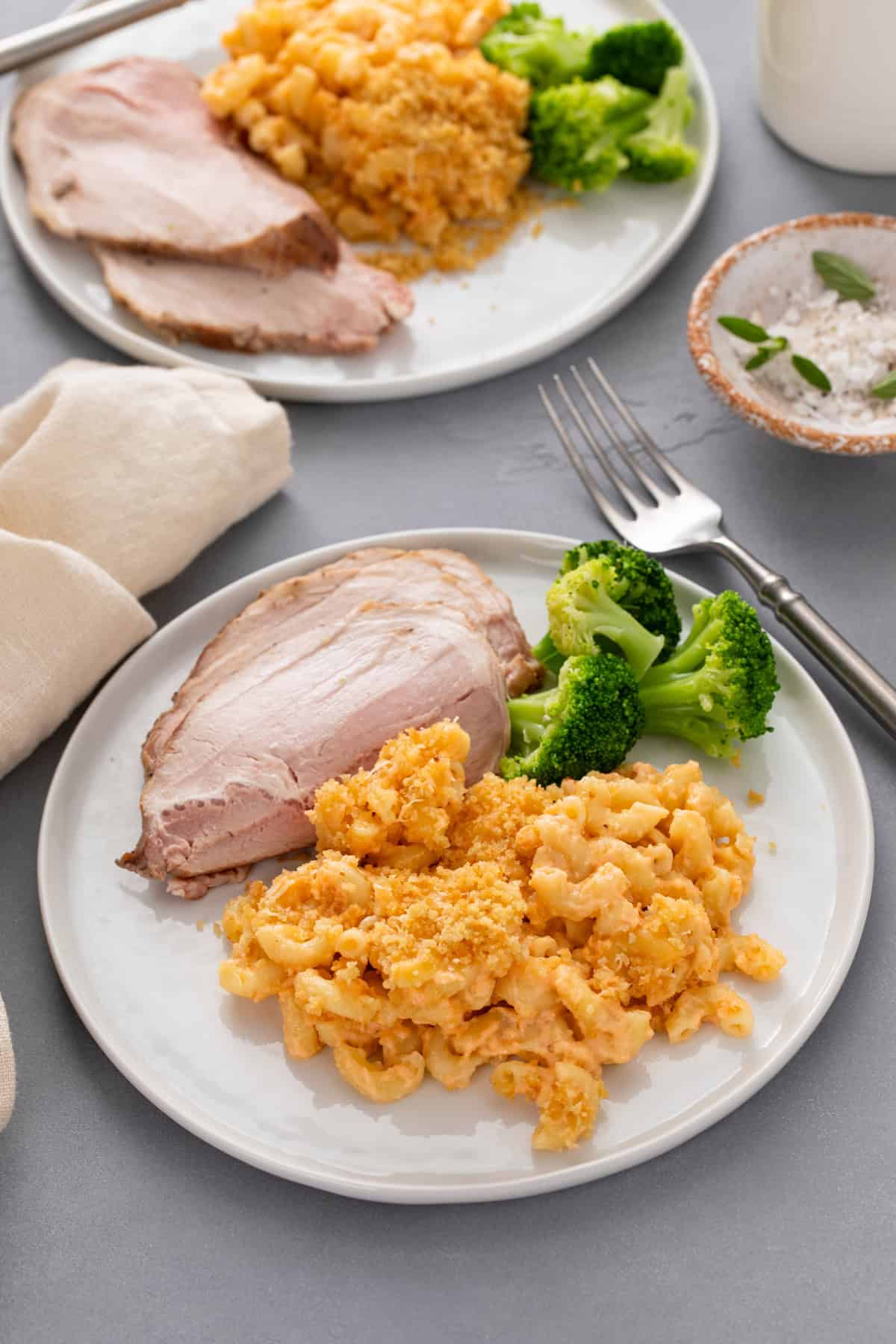 Two white plates, each holding baked macaroni and cheese next to turkey and steamed broccoli.