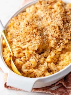 Spoon about to serve baked macaroni and cheese out of a white casserole dish