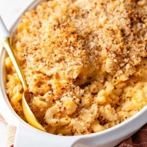 Spoon about to serve baked macaroni and cheese out of a white casserole dish