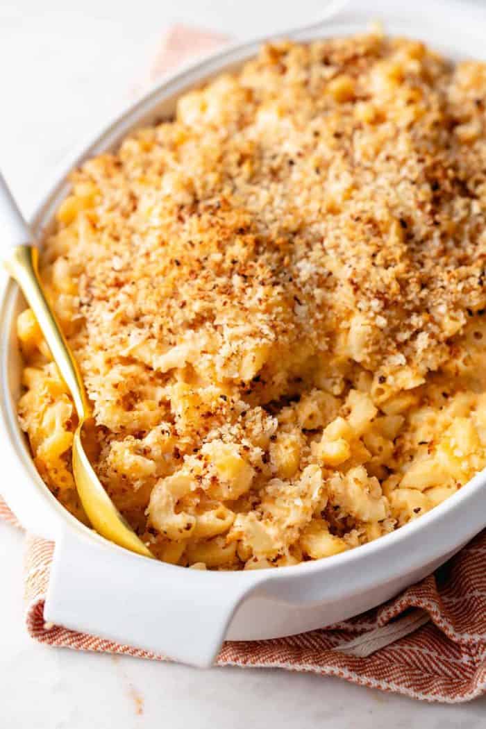 Spoon about to serve baked macaroni and cheese out of a white casserole dish