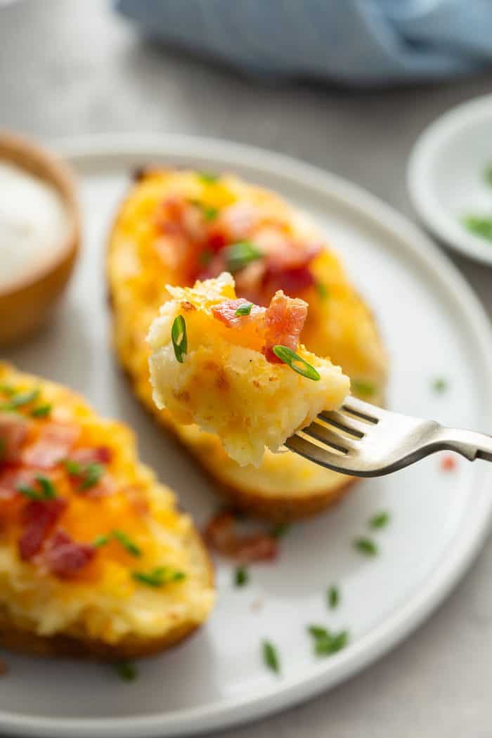 Fork holding up a bite of twice-baked potato with two twice-baked potatoes in the background