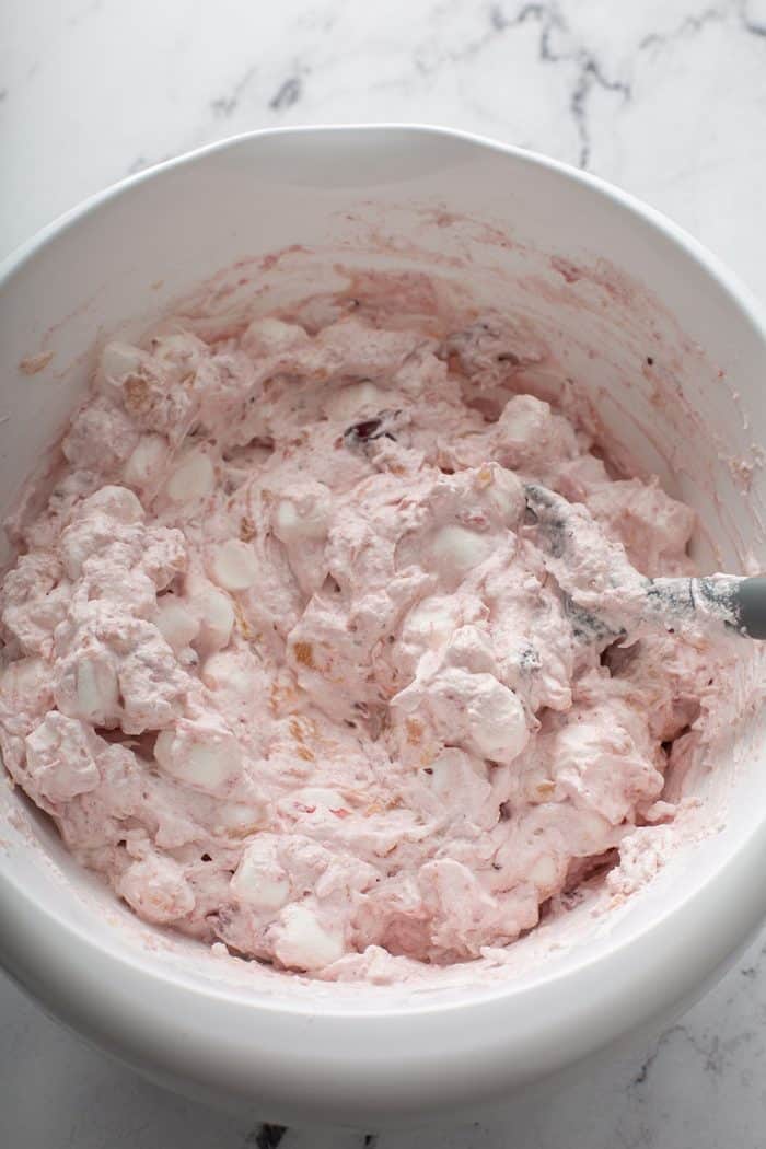 Spatula stirring together cranberry fluff in a white mixing bowl