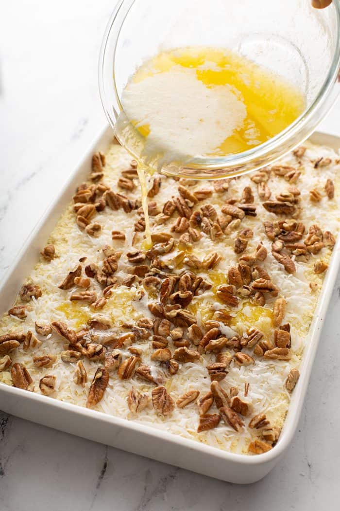 Melted butter being drizzled over cake mix, coconut, and pecans in a cake pan