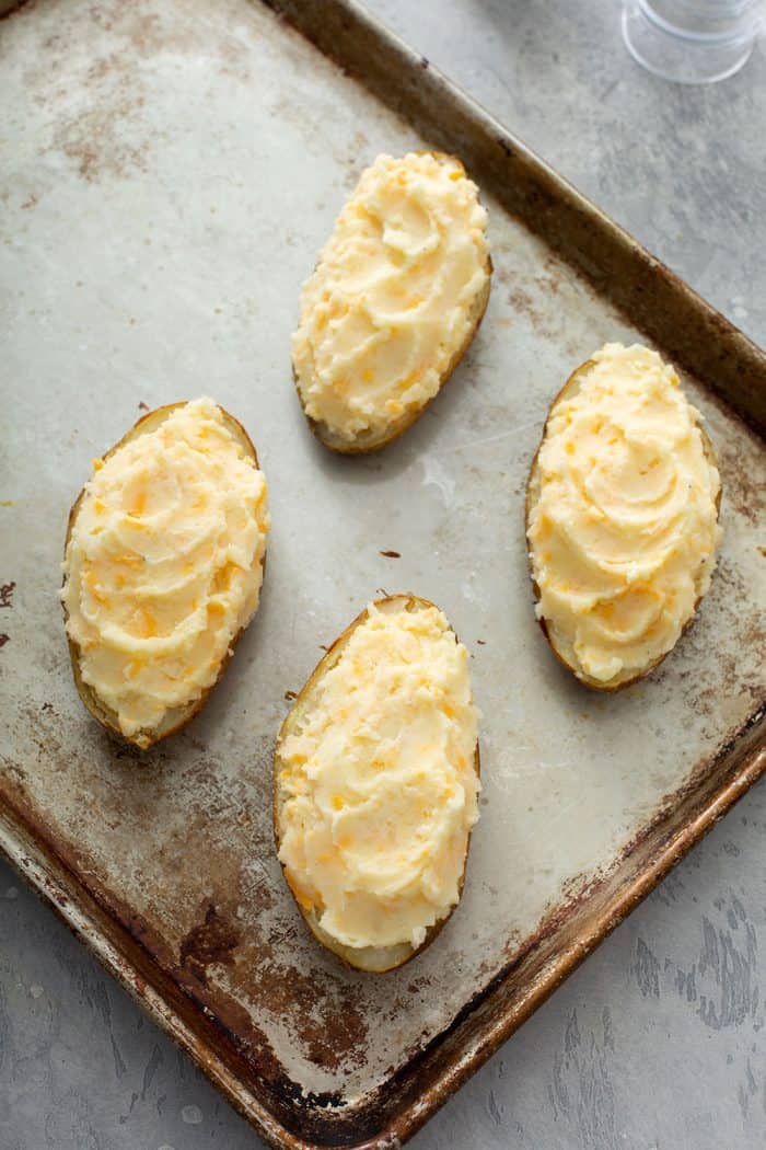 Filled twice-baked potatoes on a sheet tray, ready to be baked