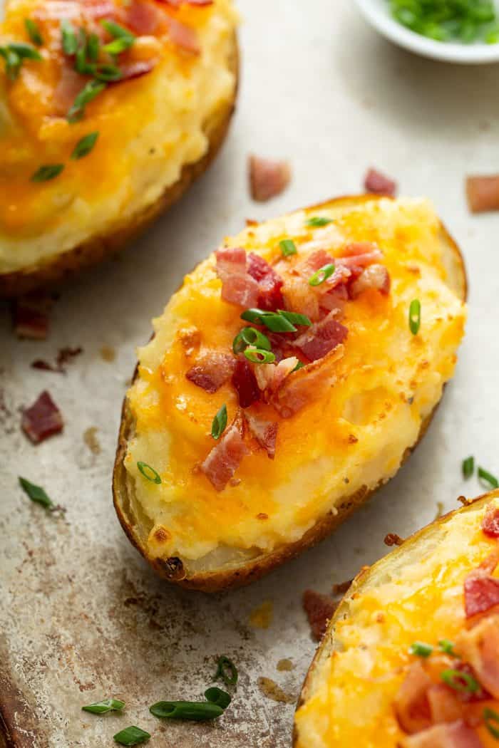 Three twice-baked potatoes lined up on a sheet tray, topped with bacon and chives