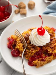 Fork about to take a bite of cherry pineapple dump cake topped with whipped cream and a cherry