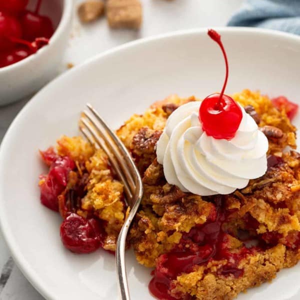 Fork about to take a bite of cherry pineapple dump cake topped with whipped cream and a cherry