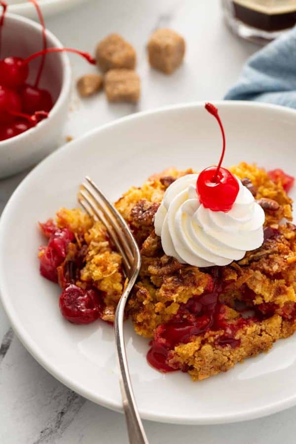 Fork about to take a bite of cherry pineapple dump cake topped with whipped cream and a cherry