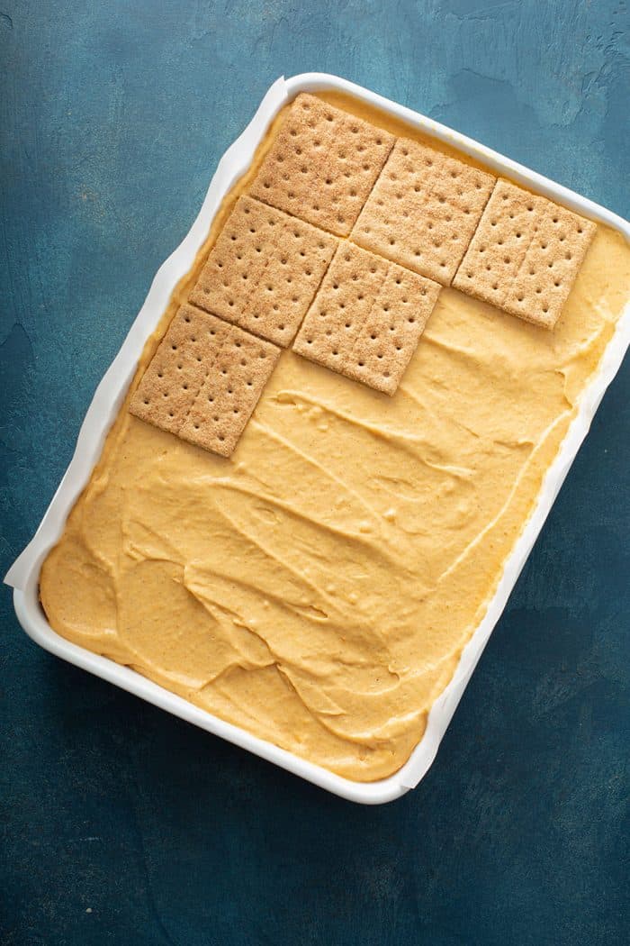 Graham crackers being layered on top of pumpkin filling in a cake pan