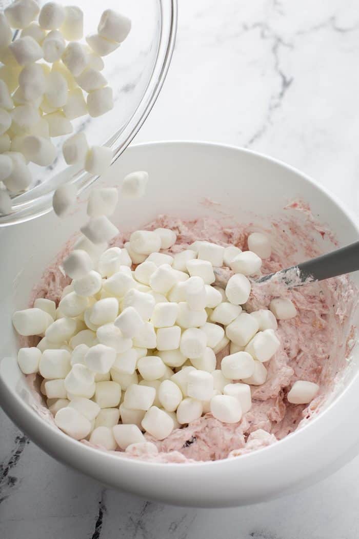 Mini marshmallows being added to a white mixing bowl