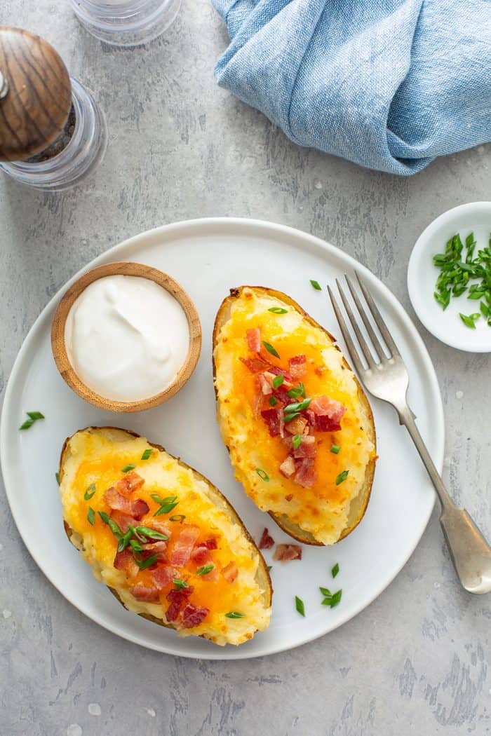 Overhead view of two twice-baked potatoes and a small bowl of sour cream arranged on a white plate