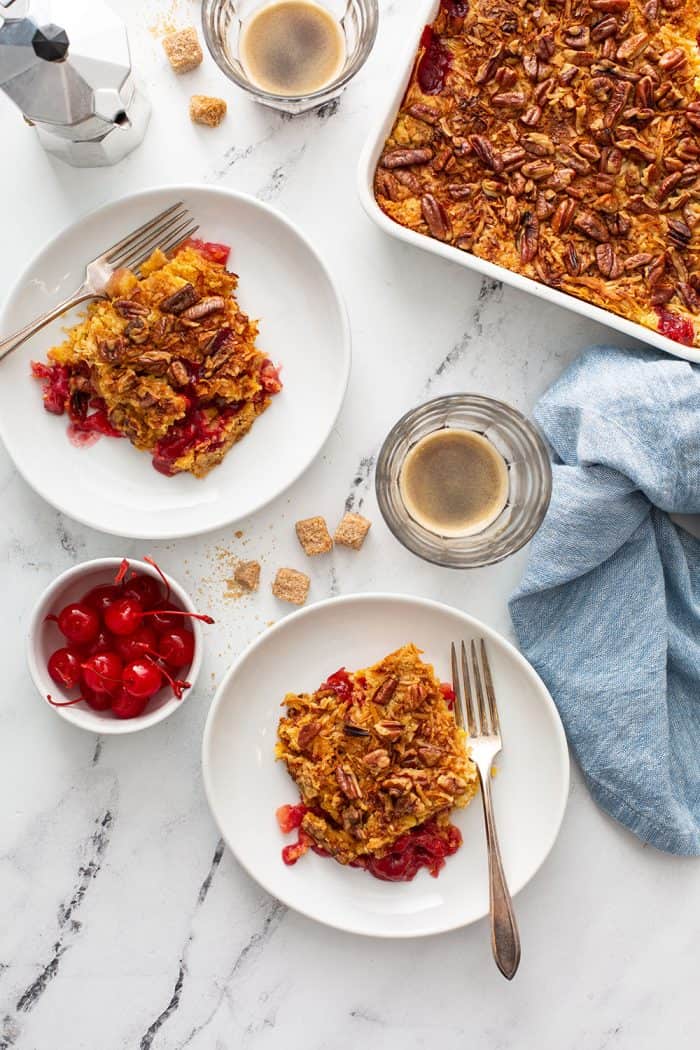 Overhead view of two white plates of cherry pineapple dump cake next to a cake pan of dump cake