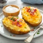 Two twice-baked potatoes, a small bowl of sour cream, and a fork on a white plate