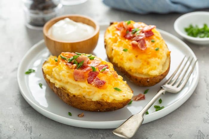 Two twice-baked potatoes, a small bowl of sour cream, and a fork on a white plate